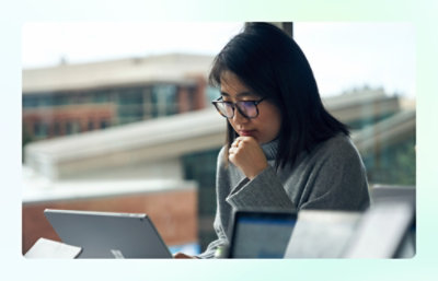 Person working on a laptop near a window overlooking buildings.