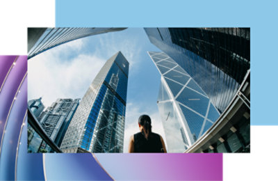 A woman looking up at towering modern skyscrapers under a clear blue sky.