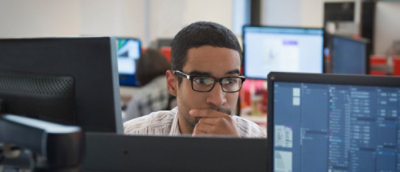 A man wearing glasses looking at a laptop.