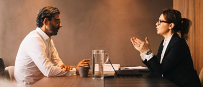 A man in a white shirt and a woman in a suit and glasses sitting at a table.