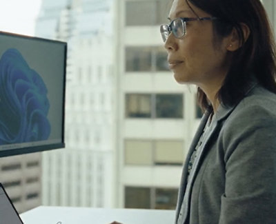 A woman wearing glasses and a grey jacket looking at a computer screen.