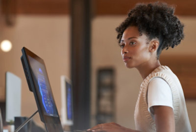 A woman with curly hair wearing a white shirt looks at a computer screen.