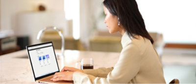 A women using a laptop at a table with a glass of red wine in an indoor setting.