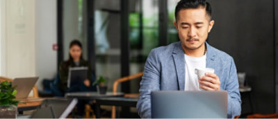 A man looking at the laptop while holding a cup of coffee
