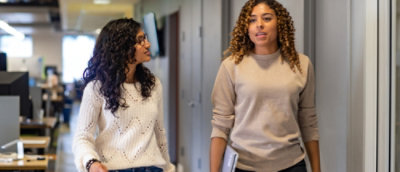 A woman with long curly hair standing next to another woman in a hallway.