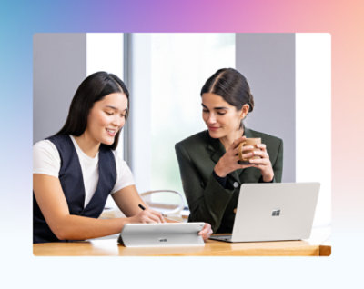 Two women sitting at a table in an office, looking at a laptop.