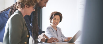 Three people in business attire are collaborating around a laptop in an office setting.