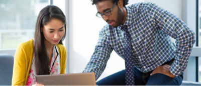 A man in a plaid shirt and a woman in a yellow cardigan looking at a laptop.