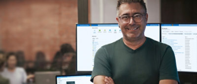 A man standing infront of two big screen desktop and smiling.