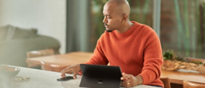 A man in an orange sweater using a laptop at a table.