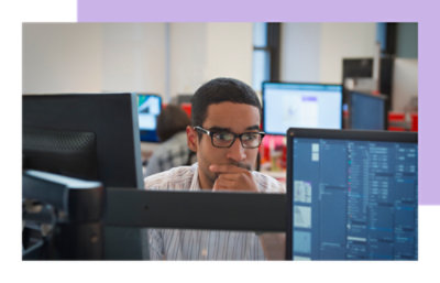 A man wearing glasses sitting at a desk, typing on a laptop