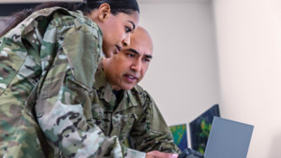  Two people in camouflage uniforms collaborating at a laptop.