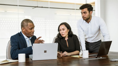 A group of people sitting around a table looking at a laptop.
