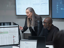 Two people reviewing information on computer monitors while working together in an office.