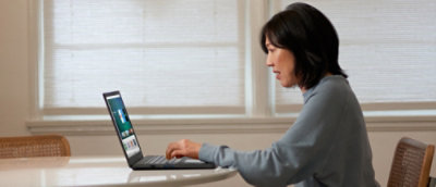 Person using laptop at table by window.