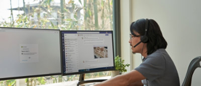 Person working at a desk with dual monitors in a bright office workspace.