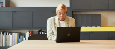 Woman in beige blazer sitting at desk looking at laptop