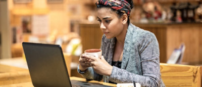 Person using laptop while holding coffee in casual indoor workspace