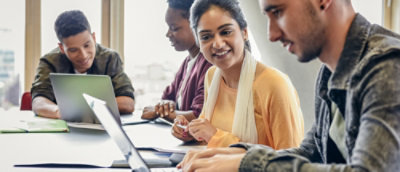 Group collaborating at a table with laptops and documents in a workspace.