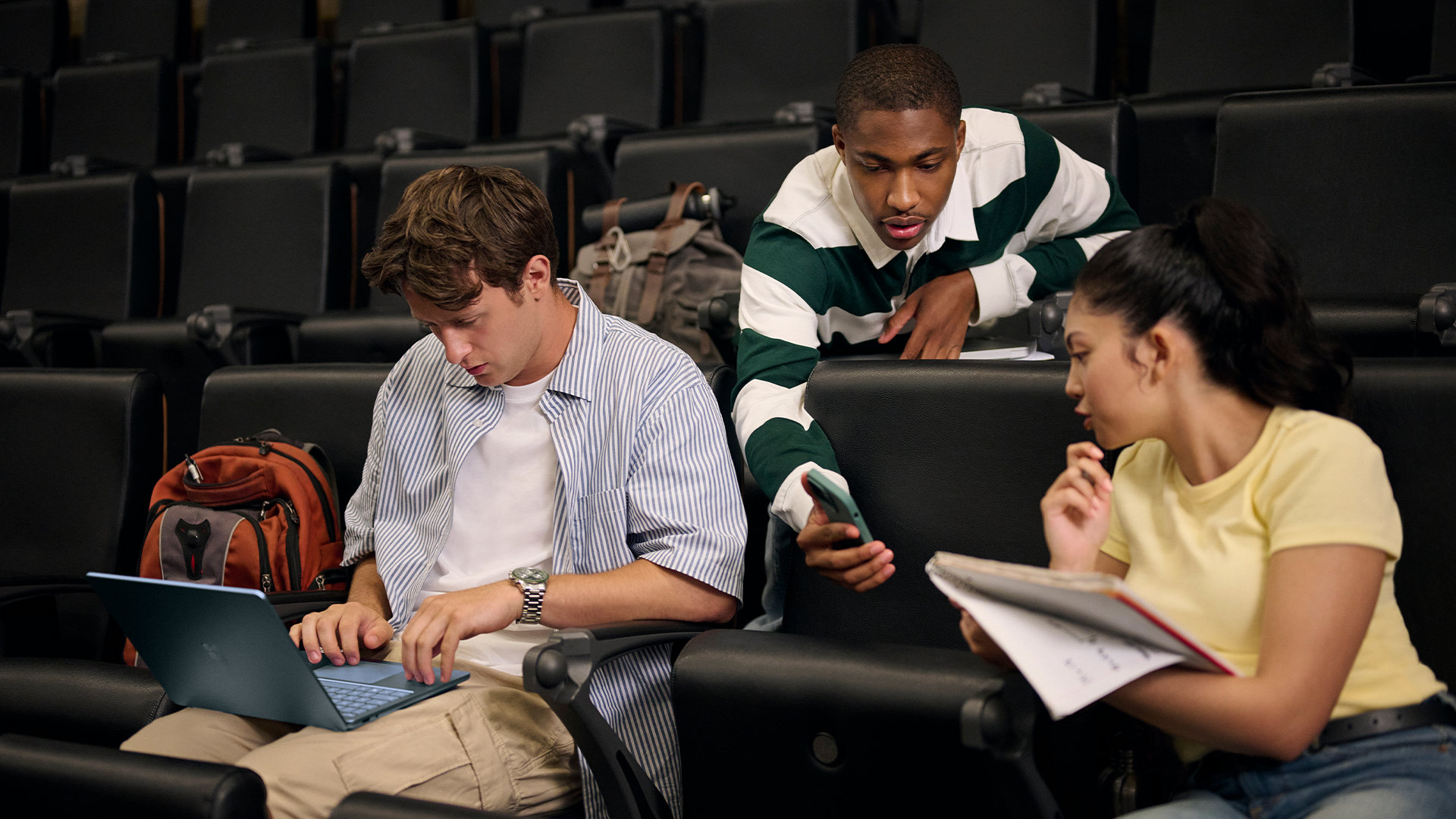 Three college students collaborate in a lecture hall with a Surface. 