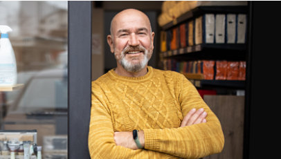 Man standing in entryway of his shop, smiling, with his arms folded.