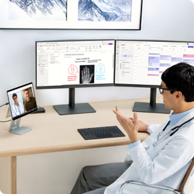 Un docteur assis à un bureau lors d’un appel vidéo utilise la caméra de la Surface Pro pour les entreprises tout en travaillant sur plusieurs écrans. 