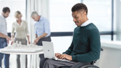 膝の上に置いた 法人向け Surface Laptop でタイピングする車椅子の人。