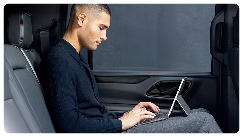 Uma pessoa sentada no banco de trás de um carro usando um Surface Pro para Empresas com o suporte Kickstand colocado, sugerindo a flexibilidade e portabilidade do dispositivo.