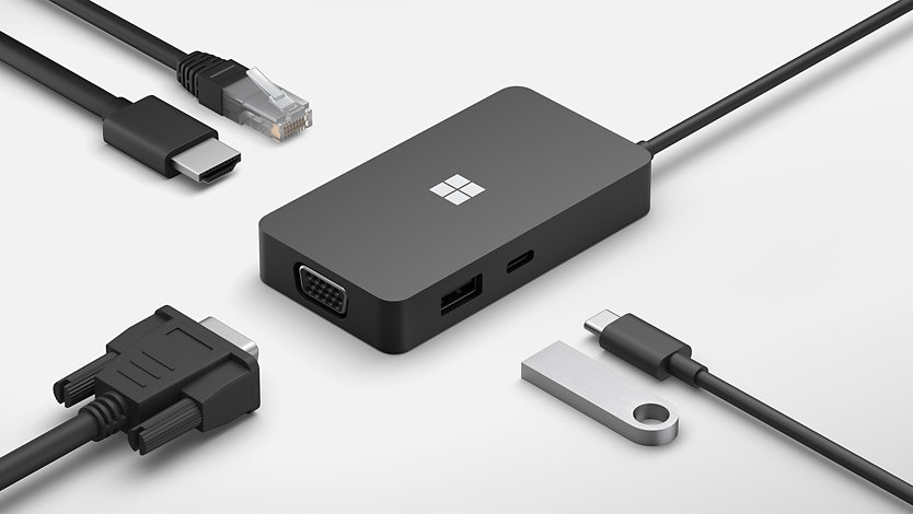 A Surface USB-C Travel Hub dock with a variety of cables and accessories to demonstrate the number and variety of attachments it supports. 