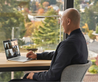 A person sits at a desk, participating in a video conference on a laptop.