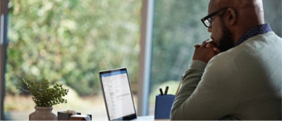 A man works on a laptop at a desk with a potted plant and stationery.