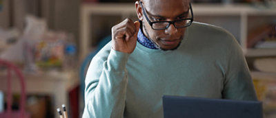 A man in a sweater looking down at a laptop