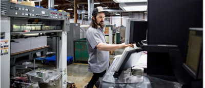 A man wearing a cap operates a control panel in an industrial setting with large