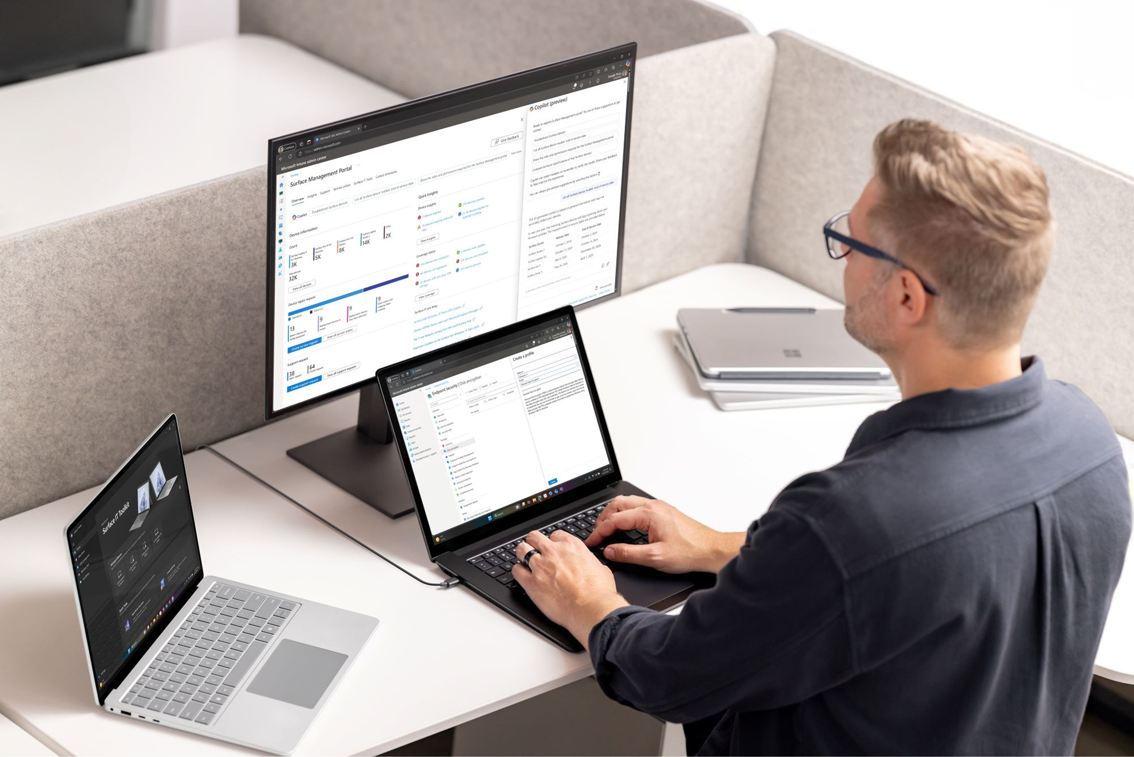 A person sitting at a desk with various devices, working on a laptop