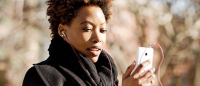 Person outdoors, dressed warmly in a black scarf and coat, looking at a smartphone. Trees and a blurred background can be seen.