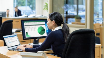 Person analyzing charts on dual monitors in an office setting.