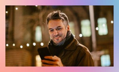 Persona sosteniendo un smartphone con luces de cadena en el fondo durante la noche.