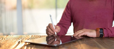 Person in a maroon shirt holding a white stylus pen near a tablet.