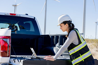 Frontline energy worker using a laptop beside a service truck near wind turbines.