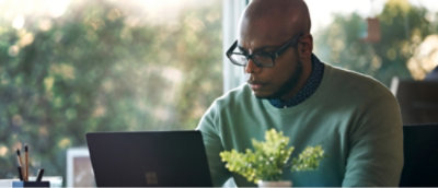 A person wearing glasses and a green sweater is focused on working at a laptop. 